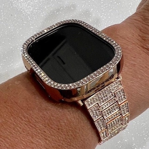 May include: A rose gold smartwatch case and matching link bracelet, both fully encrusted with small, clear, sparkling crystals. The square-shaped watch face features a dark, reflective screen surrounded by a thick, crystal-studded bezel frame.