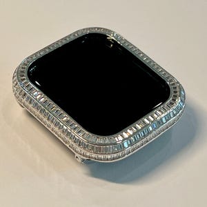 May include: A silver Apple Watch case with a diamond-encrusted bezel. The watch face is black.