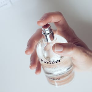 Peut inclure: Un flacon de parfum en verre transparent avec un vaporisateur argenté. Le flacon porte une étiquette sur laquelle on peut lire "parfum", "reveine", "originale" et "bergamie".