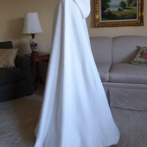 May include: A white hooded cape with a long flowing design. The cape is made of a soft, smooth fabric and has a simple, elegant style.