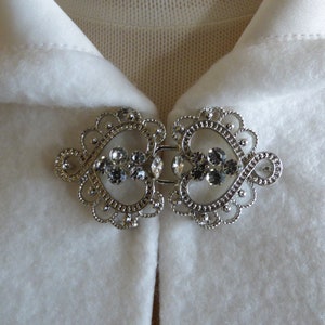 May include: A silver-toned metal clasp with a heart-shaped design and clear rhinestones. The clasp is perfect for a cape or shawl.