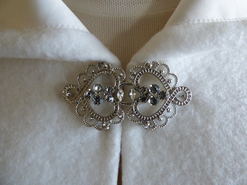 May include: A silver-toned metal clasp with a heart-shaped design and clear rhinestones. The clasp is perfect for a cape or shawl.