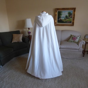 May include: A white hooded cape with a long flowing design. The cape is made of a soft, plush fabric and has a simple, elegant style.
