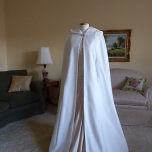 May include: A white hooded cape with a long, flowing design. The cape is made of a soft, luxurious fabric and has a simple, elegant style.