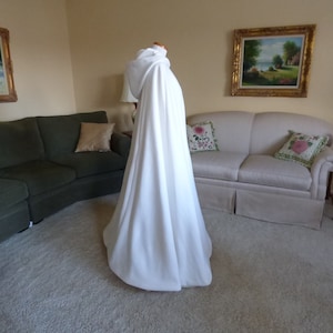 May include: A white hooded cape with a long flowing design. The cape is made of a soft, smooth fabric and has a simple, elegant style.