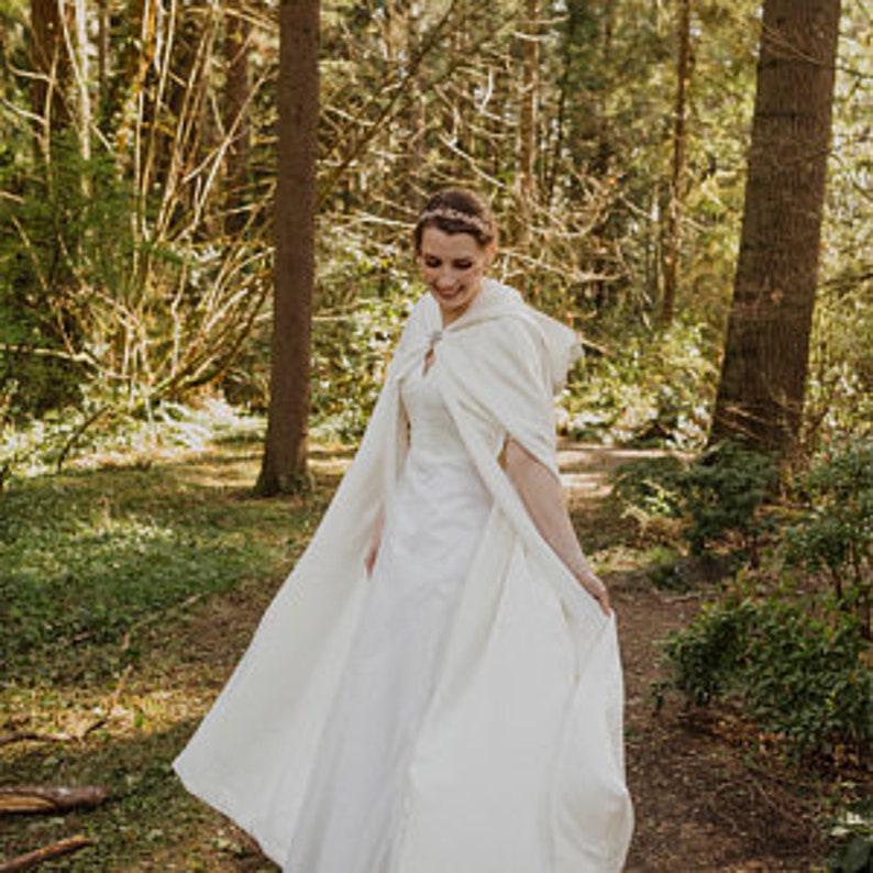 May include: A white hooded cape with a long train, worn by a person in a forest setting.