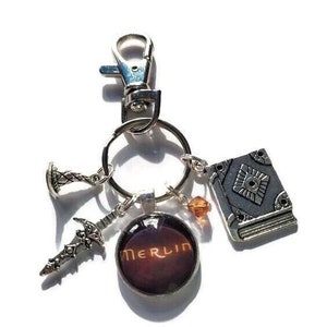 Puede incluir: Un llavero de plata con un dije que dice "Merlin" en rojo oscuro y naranja. El llavero tambi&eacute;n tiene una peque&ntilde;a espada de plata, un dije de libro de plata y un peque&ntilde;o dije de corona de plata.
