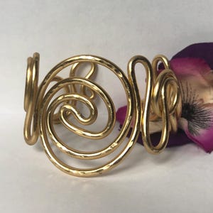 May include: A gold-toned metal bracelet with a hammered finish and a swirling, abstract design.