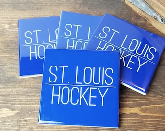 May include: Four blue square coasters with white text. The text on the coasters reads "ST. LOUIS HOCKEY".
