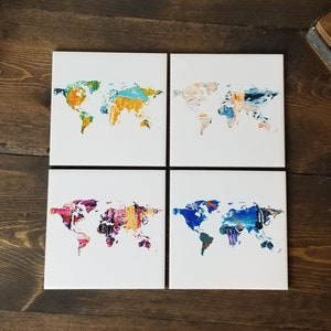 May include: Set of four ceramic coasters featuring a world map design. Each coaster has a different abstract paint design in shades of blue, yellow, orange, pink, and purple.