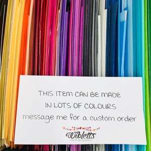 May include: A close-up of a variety of colored cardstock paper samples. The text on the white card reads: "THIS ITEM CAN BE MADE IN LOTS OF COLOURS message me for a custom order Wibletts event decorations"
