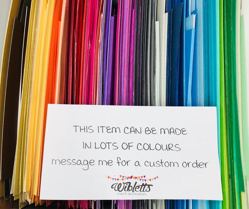May include: A close-up of a variety of colored cardstock paper samples. The text on the white card reads: "THIS ITEM CAN BE MADE IN LOTS OF COLOURS message me for a custom order Wibletts event decorations"