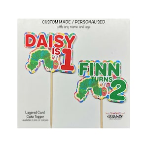 May include: Two personalized The Very Hungry Caterpillar cake toppers. The first topper says "Daisy is 1" with a green caterpillar and a red number 1. The second topper says "Finn Turns 2" with a green caterpillar and a green number 2.