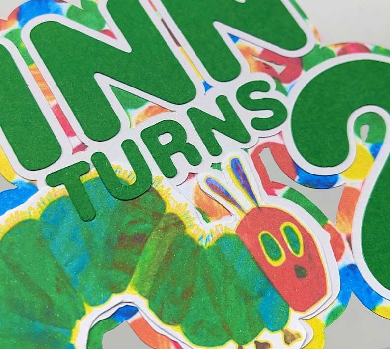 May include: Green paper cutouts of the words "Finn turns 2" with a colorful caterpillar illustration.