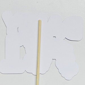 May include: White paper cutout of the word "You're" with a wooden stick attached to the back.