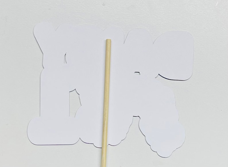 May include: White paper cutout of the word "You're" with a wooden stick attached to the back.