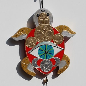 May include: A red, white and gold painted wooden turtle with a large blue eye and a silver pentagram. The turtle is hanging from a string with beads and feathers.