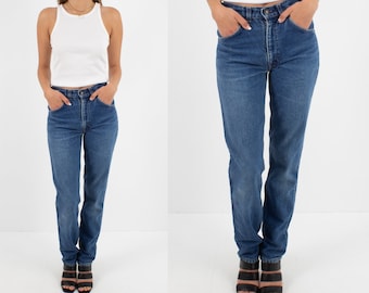 May include: A pair of blue denim jeans with a high waist and straight leg fit. The jeans are shown on a model wearing a white tank top and black sandals.