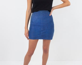 May include: A woman wearing a black t-shirt and a blue denim mini skirt with a crocodile print. She is wearing leopard print sliders.
