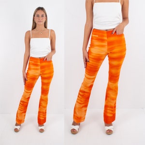 May include: A woman is wearing a white vest top and orange flared trousers with a tie-dye pattern. She is wearing white sandals.