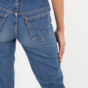 May include: A pair of blue denim jeans with a high waist and a straight leg. The jeans have a classic five-pocket style and a faded wash.