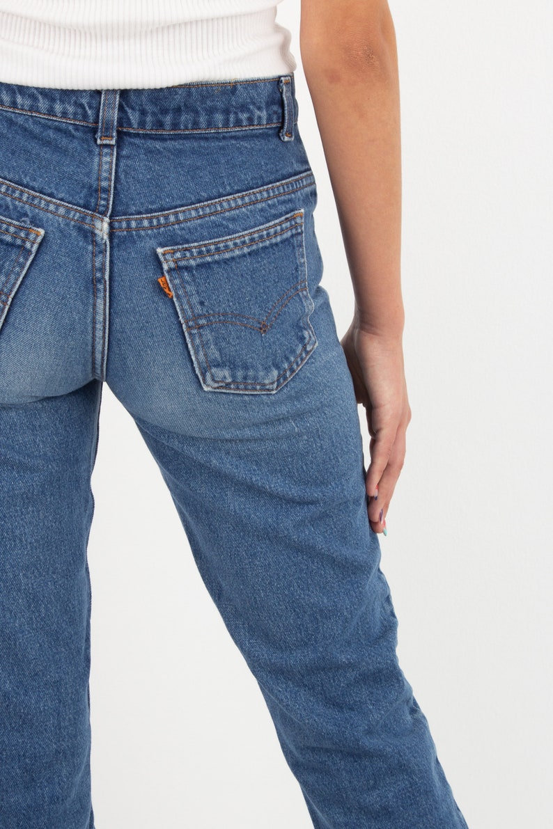 May include: A pair of blue denim jeans with a high waist and a straight leg. The jeans have a classic five-pocket style and a faded wash.