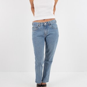 May include: A woman is wearing a white tank top and light blue denim jeans. She is wearing black heeled sandals.