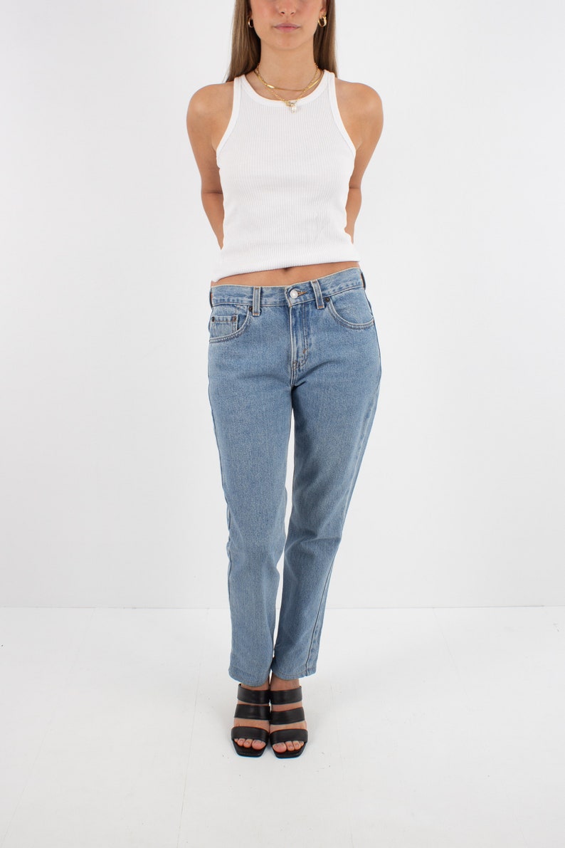 May include: A woman is wearing a white tank top and light blue denim jeans. She is wearing black heeled sandals.