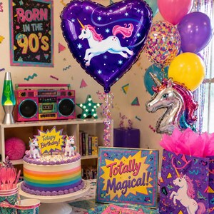 May include: A birthday party setup featuring a purple heart-shaped unicorn balloon, a round cake with rainbow stripes and a Totapy Birthday topper, a Totally Magical sign, a unicorn gift bag, and colorful balloons in a 90s themed room.
