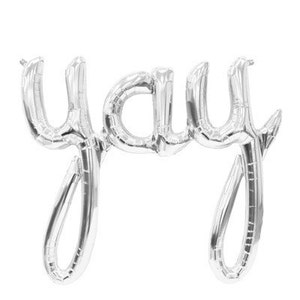 Puede incluir: Un globo de papel de aluminio plateado con la palabra "yay" en cursiva. El globo está inflado y tiene un acabado brillante y metálico. El fondo es blanco.