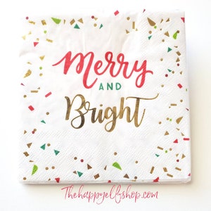 May include: White paper napkins with a gold and red confetti pattern. The text "Merry and Bright" is written in gold and red lettering.