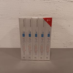 May include: A stack of five Memorex VHS videotape boxes. Each box is white with black and blue text, including "120 Minute" and "VHS VideoTape." The top box has a red and white "5PK" label.