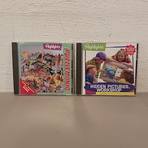 May include: Two CD-ROMs of Highlights children's activity games. One is titled "Puzzlemania" with a colorful illustration of a theme park. The other is "Hidden Pictures Workshop" with children looking at a screen. Both are in black CD cases.