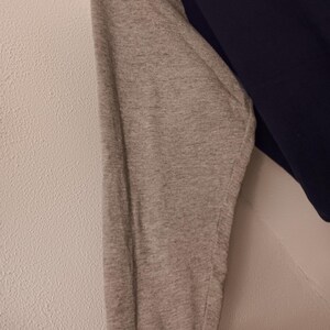 May include: A navy blue and gray long-sleeved shirt. The gray sleeve has a ribbed cuff with red and white stripes. The shirt is made of a soft material.