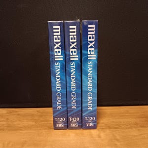 May include: Three Maxell Standard Grade T-120 VHS video cassette tapes. The blue and white boxes are stacked vertically. The text on the boxes includes "maxell", "STANDARD GRADE", "T-120", "246m", and "VHS".