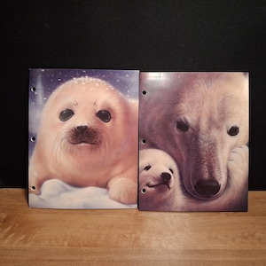 May include: Two rectangular binder covers featuring wildlife illustrations. The left cover displays a light-colored harp seal pup on snow. The right cover shows an adult polar bear with a cub. Both covers have three circular holes along the left edge.