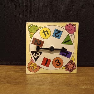 May include: Vintage children's game with a spinning wheel featuring numbers and shapes. The wheel is surrounded by cartoon animal illustrations. The numbers are in various colors, and the game is on a yellow background.