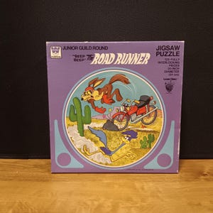 May include: A vintage Road Runner jigsaw puzzle box. The purple box features a circular image of the Road Runner and Wile E. Coyote with a motorcycle and cacti. The puzzle has 125 pieces and a 20-inch diameter.