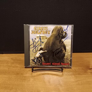 May include: A Circus Wolfboy CD titled beast sized heart in a clear plastic jewel case. The cover art features a person sitting on a stool next to a large elephant in a field, with multiple black ink signatures written across the front surface.