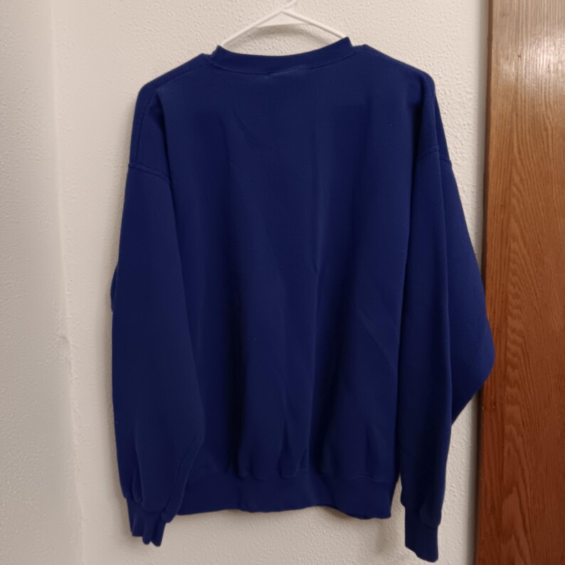 Pode incluir: Um moletom azul marinho liso pendurado em um cabide branco. O moletom tem gola redonda e mangas compridas com punhos e bainha canelados. A pe&ccedil;a &eacute; feita de um material macio e espesso.