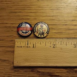 May include: Two vintage pinback buttons with text and illustrations. One reads "CLEAN UP & PAINT UP" and "The Modern Crusader." The other says "MODERN HEALTH CRUSADER." A wooden ruler with "MADE IN U.S.A." is below the buttons.