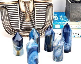Pode incluir: Uma coleção de seis pontas de cristal de ágata azul e branca. Os cristais têm uma superfície polida com padrões de faixas azuis e brancas. Os cristais são exibidos em frente a um busto egípcio. Os cristais têm cerca de 7-10 cm de altura.