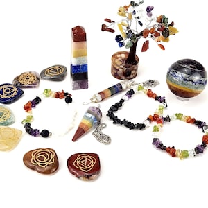 May include: An assortment of chakra-themed items, including bracelets, pendants, and stones. A multi-colored crystal tree and a striped sphere are also present. The items are arranged on a white surface.