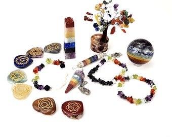 May include: An assortment of chakra-themed items, including bracelets, pendants, and stones. A multi-colored crystal tree and a striped sphere are also present. The items are arranged on a white surface.
