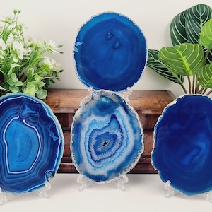 May include: Four blue agate coasters with unique patterns and a polished finish. Each coaster is a different shade of blue, with white and gray accents. They are displayed on clear stands, showcasing their natural beauty.
