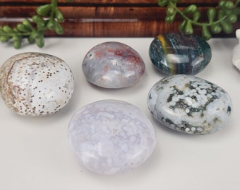 Puede incluir: Cinco piedras pulidas en varios colores y patrones. Las piedras incluyen blanco con puntos marrones, gris con rojo, verde con amarillo, blanco con negro y morado claro. Las piedras son lisas y de forma ovalada.
