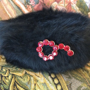 May include: A black fur hat with a red rhinestone key-shaped embellishment.