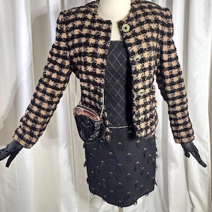 May include: A vintage ensemble featuring a black and tan checkered jacket with gold buttons, paired with a black dress. A small, beaded purse hangs from the jacket. The dress has a diamond pattern on the bodice and a fringed skirt. Black gloves complete the look.