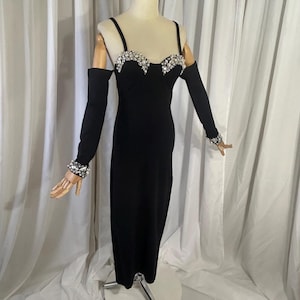 May include: A black evening dress with a sweetheart neckline and spaghetti straps. The bodice is embellished with sparkling rhinestones. Long black sleeves with rhinestone cuffs are included. The dress is displayed on a mannequin.