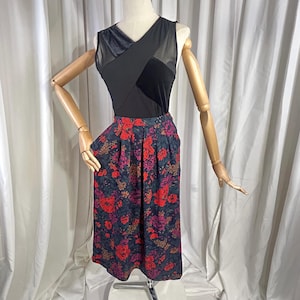 May include: A black sleeveless top with a velvet and mesh design, paired with a knee-length skirt. The skirt features a dark background with a vibrant floral pattern in red, pink, and green.